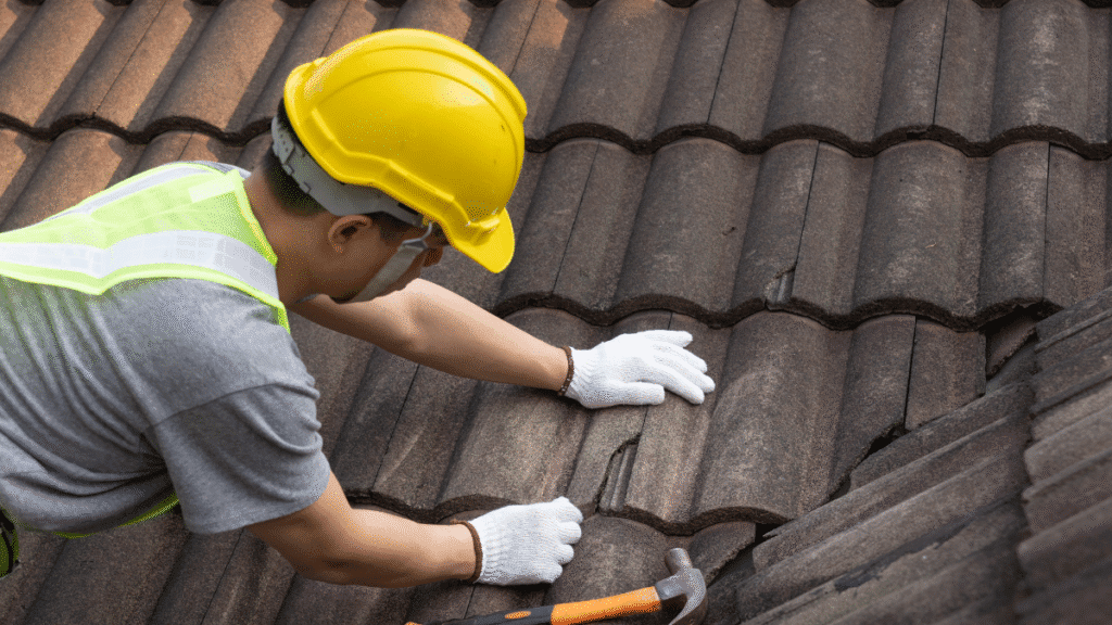 Roofer in a yellow hat performing urgent roof repair on a cracked tile roof in Tampa.