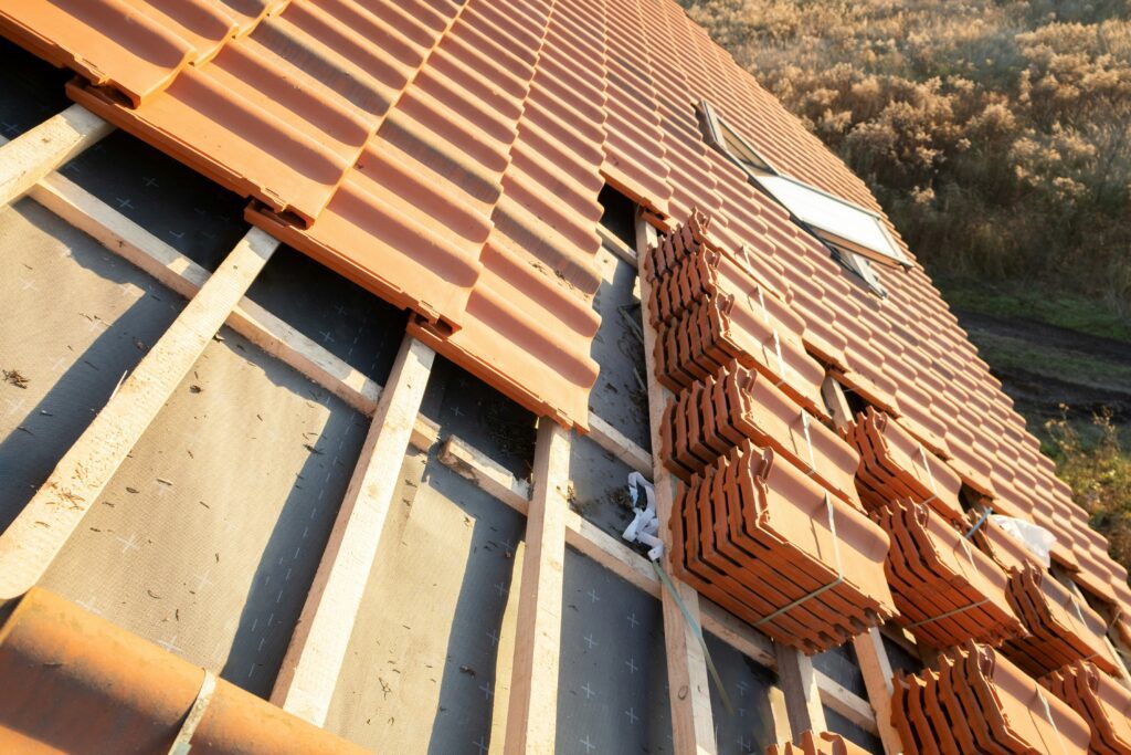 A roof under construction, showing roof tiles being installed over wooden battens and black underlayment.