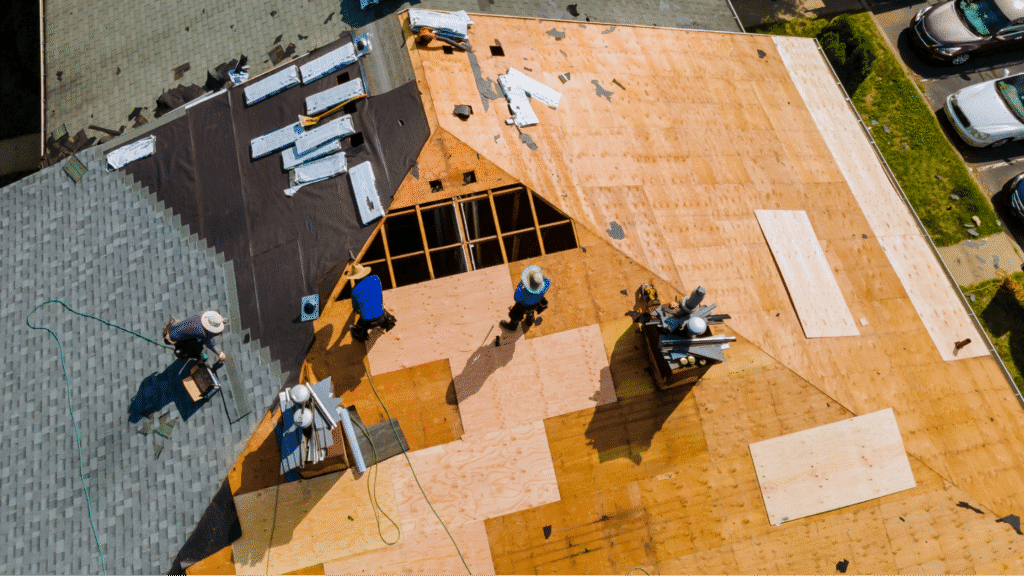 Aerial view of a professional roofing crew installing new plywood sheathing on a residential home during a roof replacement project.