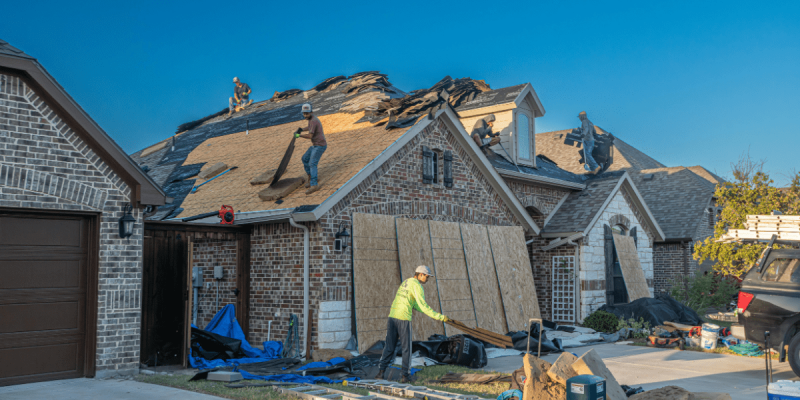 A team of roofers from Fix Roofing LLC installing new shingle material onto a large residential home during a roof replacement project.