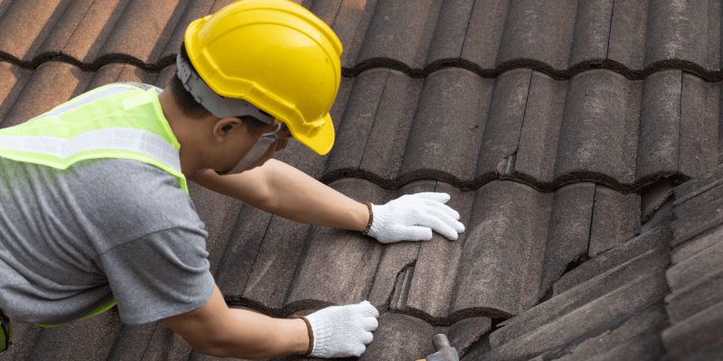 Roofer in a yellow hat performing urgent roof repair on a cracked tile roof in Tampa.
