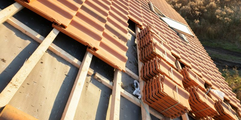 A roof under construction, showing roof tiles being installed over wooden battens and black underlayment.