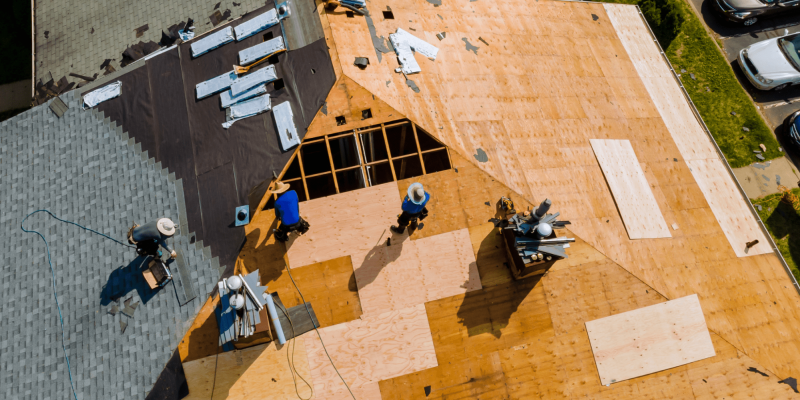 Aerial view of a professional roofing crew installing new plywood sheathing on a residential home during a roof replacement project.
