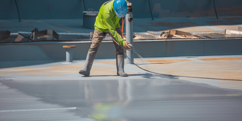 Construction worker applying protective roof coating to improve durability